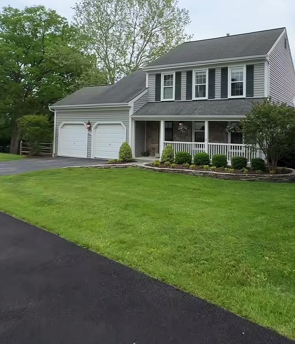 Grey colonial home with black shutters, two-car garage and a wide green lawn