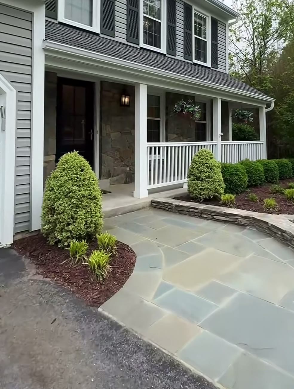 Covered front porch with white railings and a flagstone walkway lined with shrubs