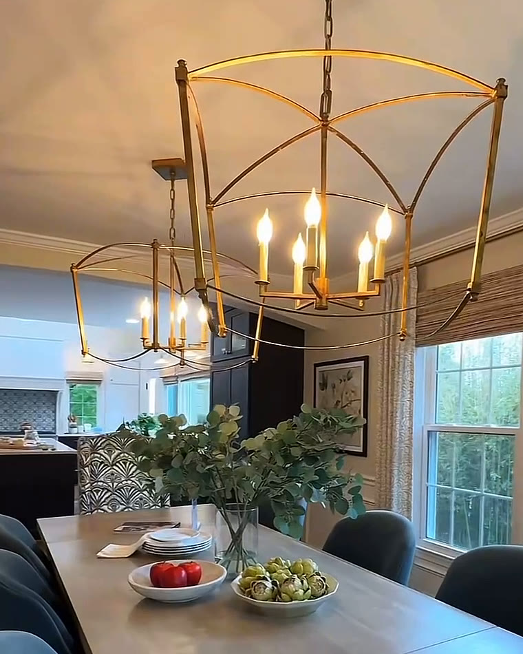 Dining room with brass lantern chandeliers over a long table and blue velvet chairs, open to the kitchen
