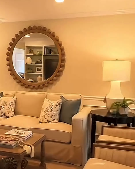 Living room with a round wooden mirror, linen sofa and table lamp