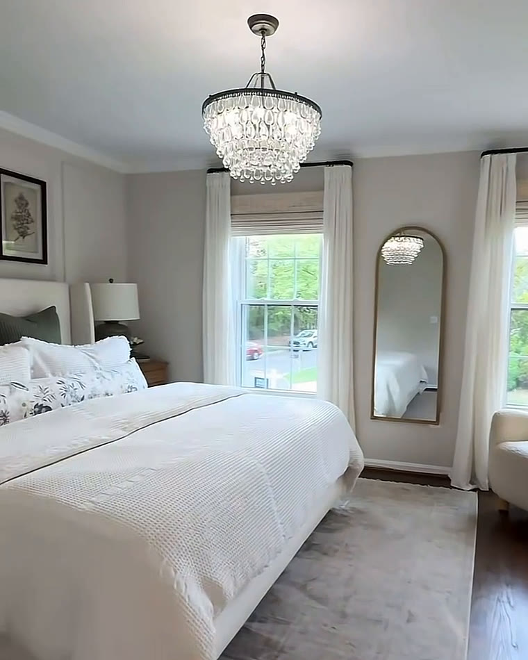 Bright bedroom with a crystal chandelier, white bedding and a tall arched mirror