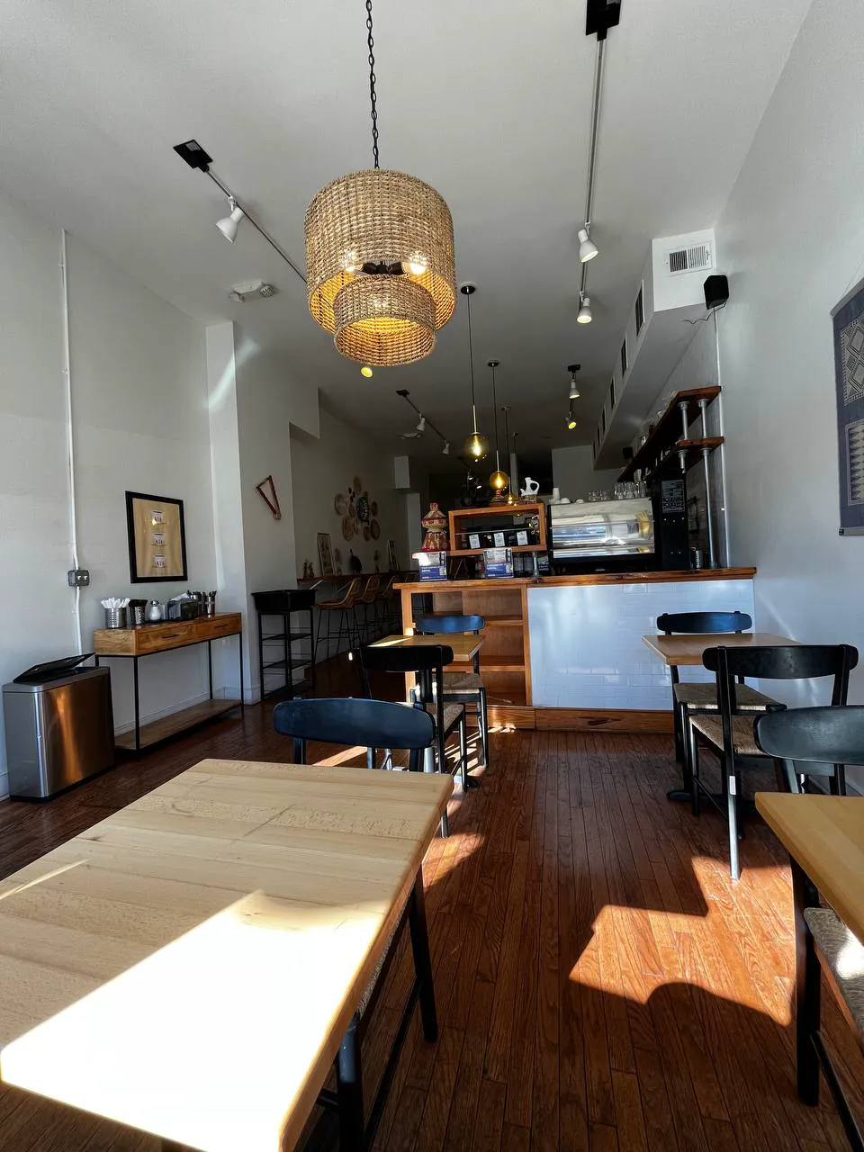 The long dining room under a woven pendant lamp, with the bar at the far end