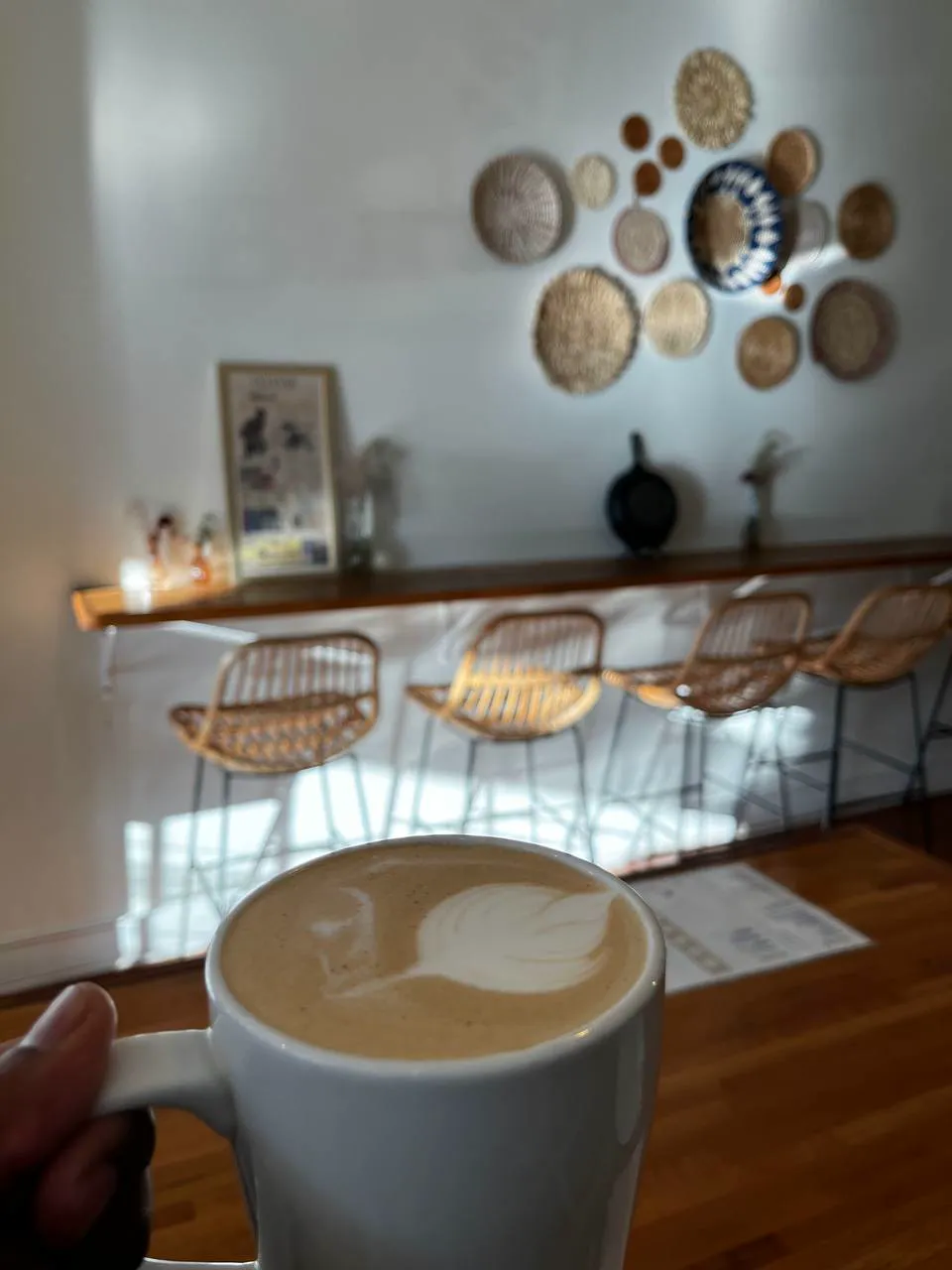 A latte with a tulip of foam, held up in front of the woven-basket wall