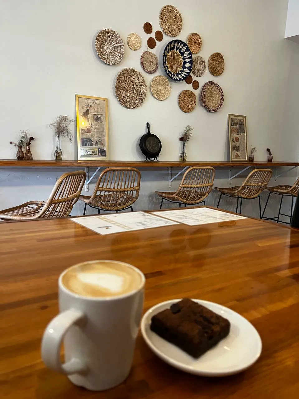 A brownie on a small white plate beside a latte