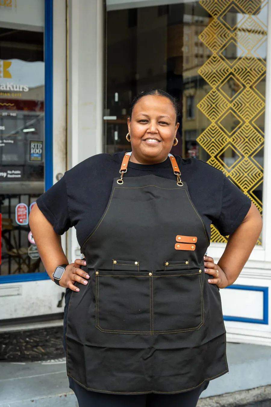 Lily Fasil, founder of Buna Kurs, smiling in a black apron outside the café