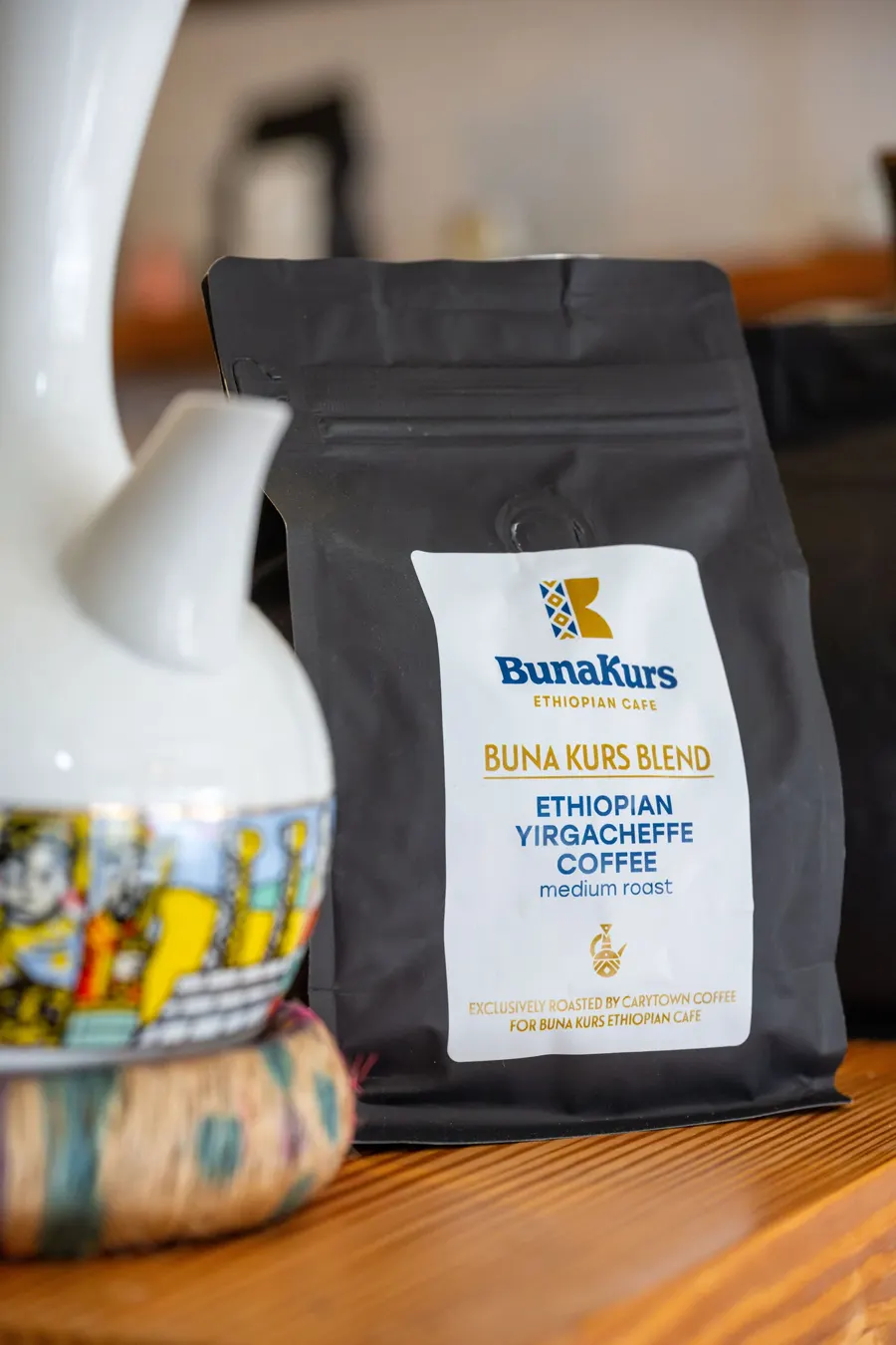 A bag of Buna Kurs Blend Ethiopian Yirgacheffe coffee beside a white clay jebena