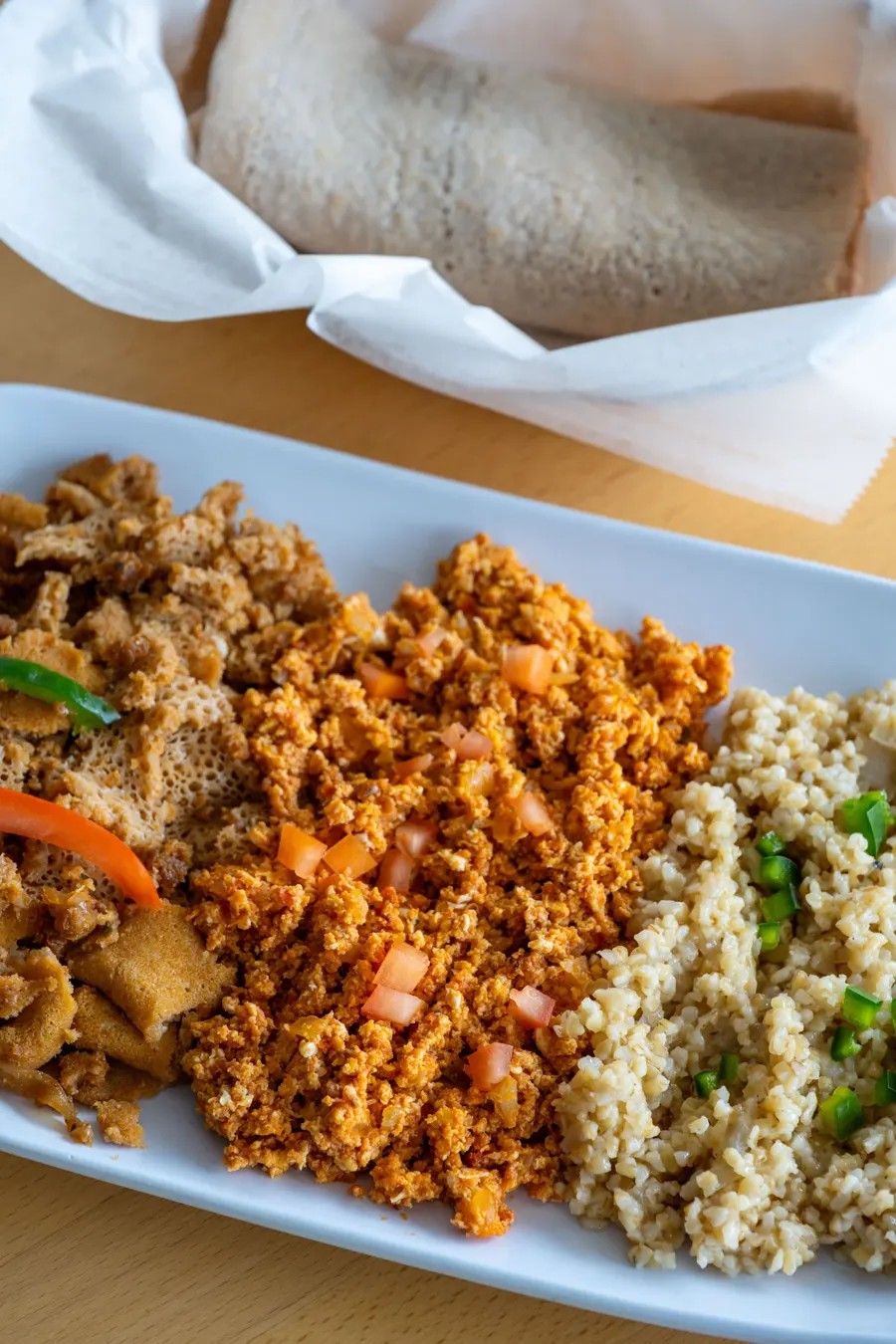 The breakfast combo: fir fir, egg silsi and kinche on a white platter with rolled injera