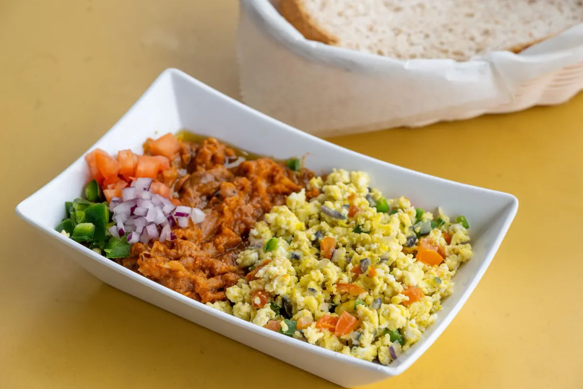 Fu'ul with scrambled eggs, garnished with tomato, onion and jalapeño, with a basket of bread