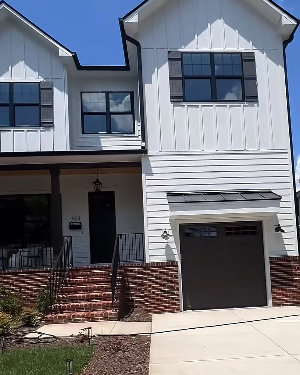 White modern farmhouse-style new build with black windows, a brick stoop and a front-facing garage