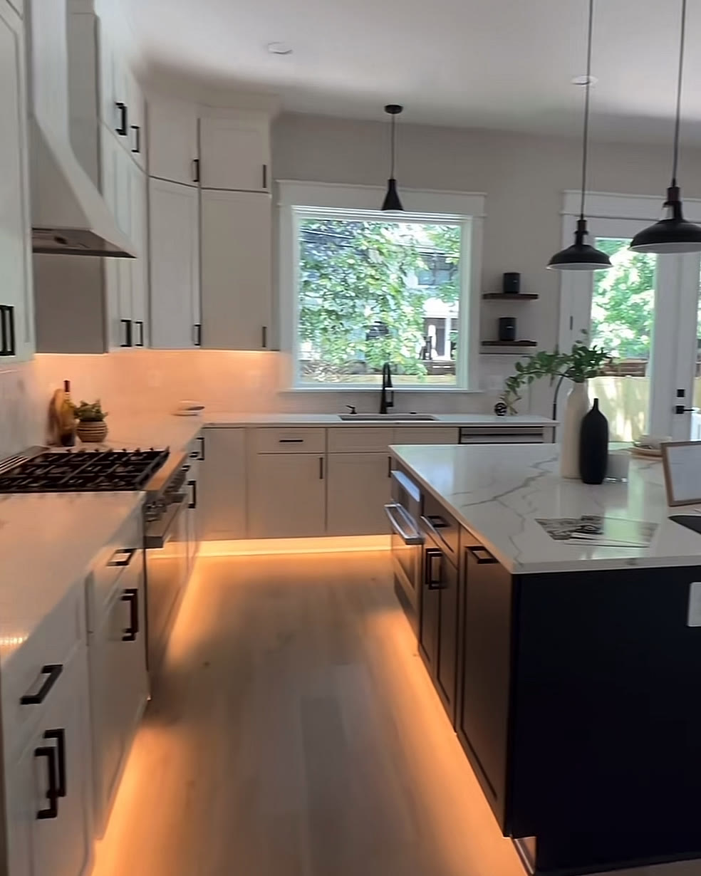 Kitchen with warm under-cabinet lighting, a black island and pendant lights