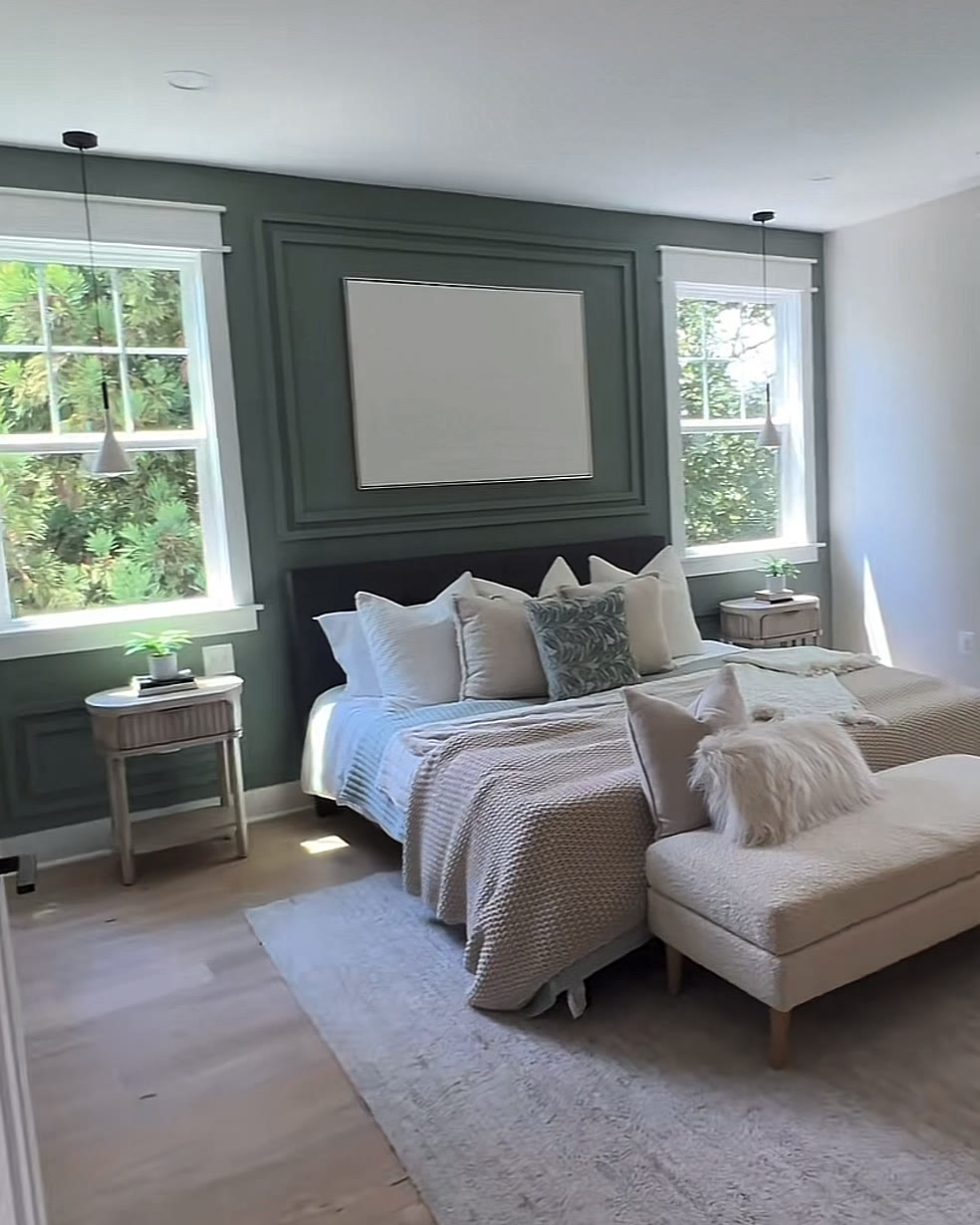 Primary bedroom with a deep green accent wall, upholstered bed, bench and wide windows