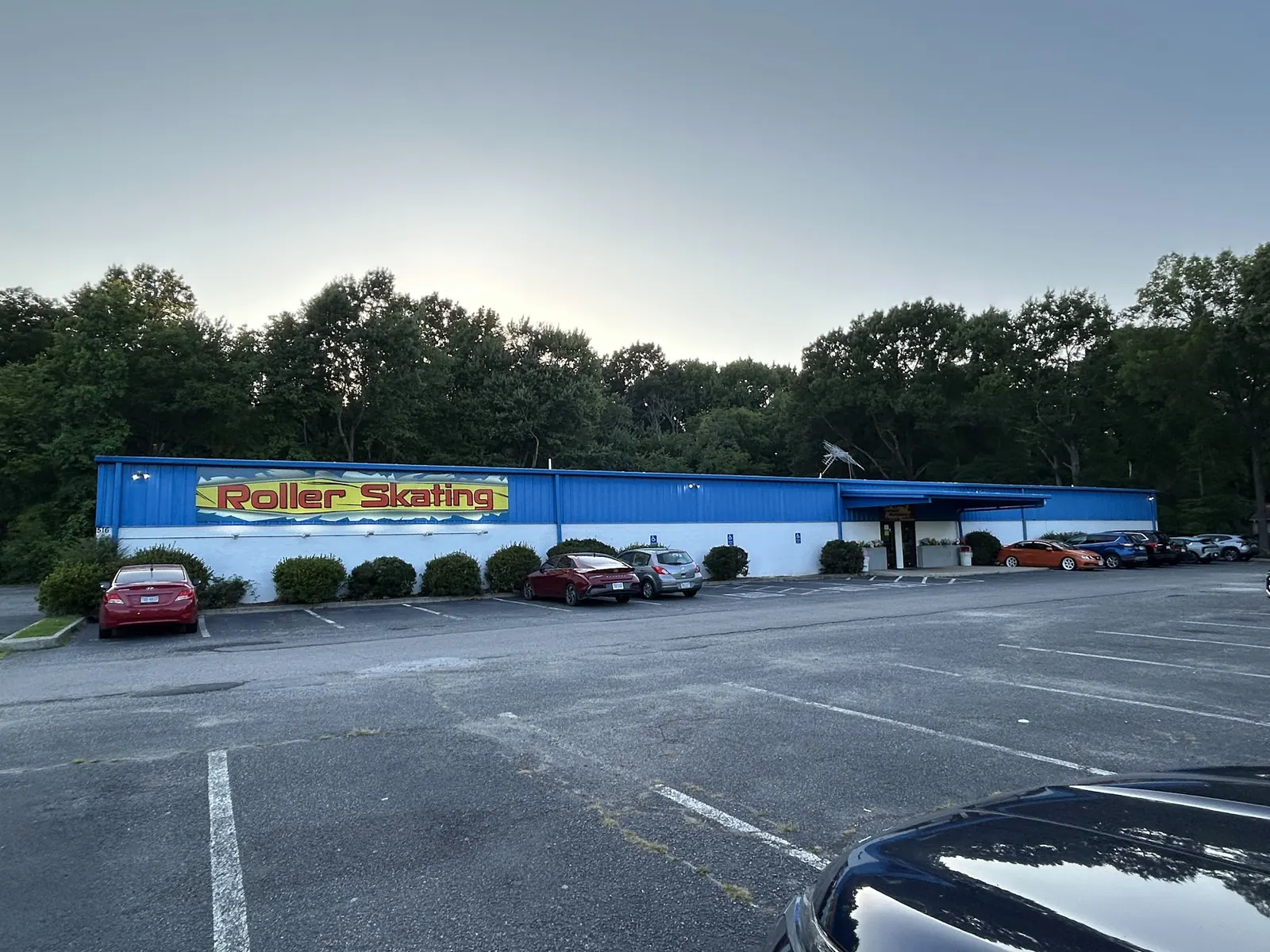 The long blue Skateland building with its red-and-yellow Roller Skating sign, seen across the parking lot at dusk.