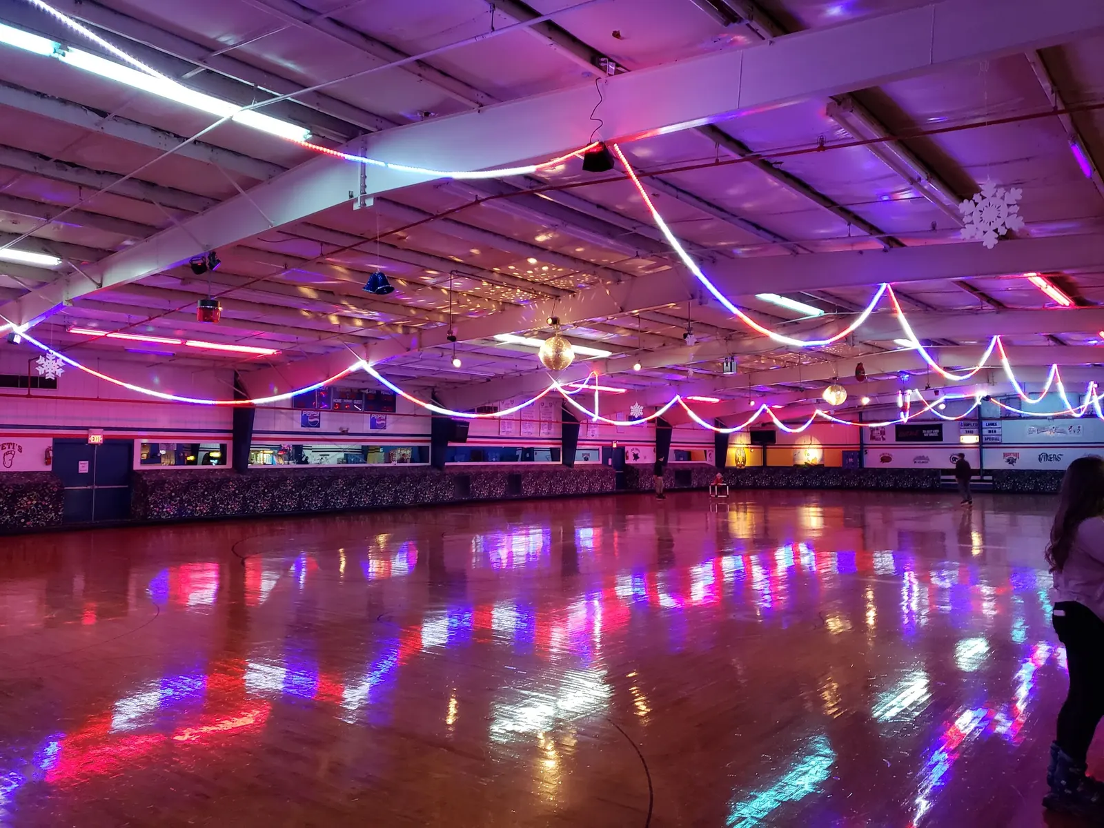 The rink floor reflecting pink, white and blue rope lights strung across the ceiling, with a disco ball.