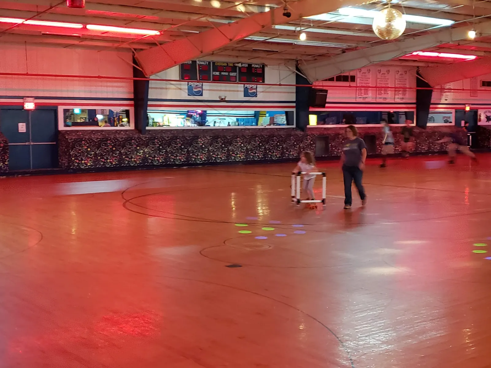 A child pushing a Skate Mate walker across the rink with a parent alongside.