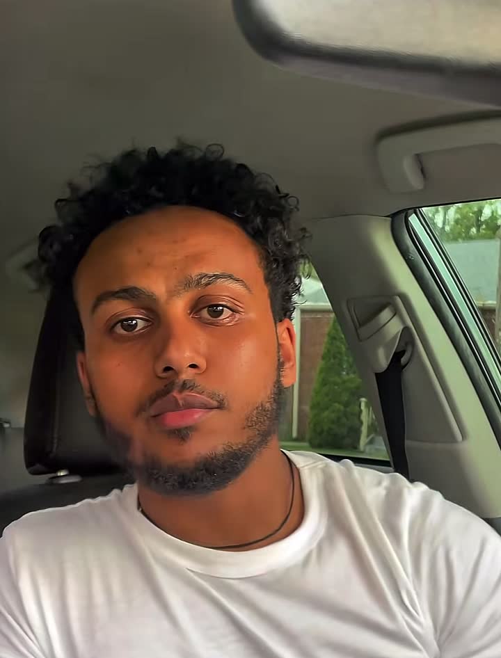 Teddy, the locksmith, in a white T-shirt talking to the camera from the driver’s seat of a car.